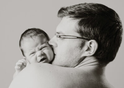 Pai beija bebé recém-nascido no ombro — Humberto Barbosa capta sessão newborn a preto e branco em São João da Madeira