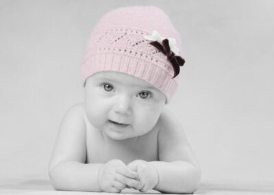Bebé com gorro rosa e laços deitado em pose terna captado por Humberto Barbosa em São João da Madeira — fotografia newborn a preto e branco