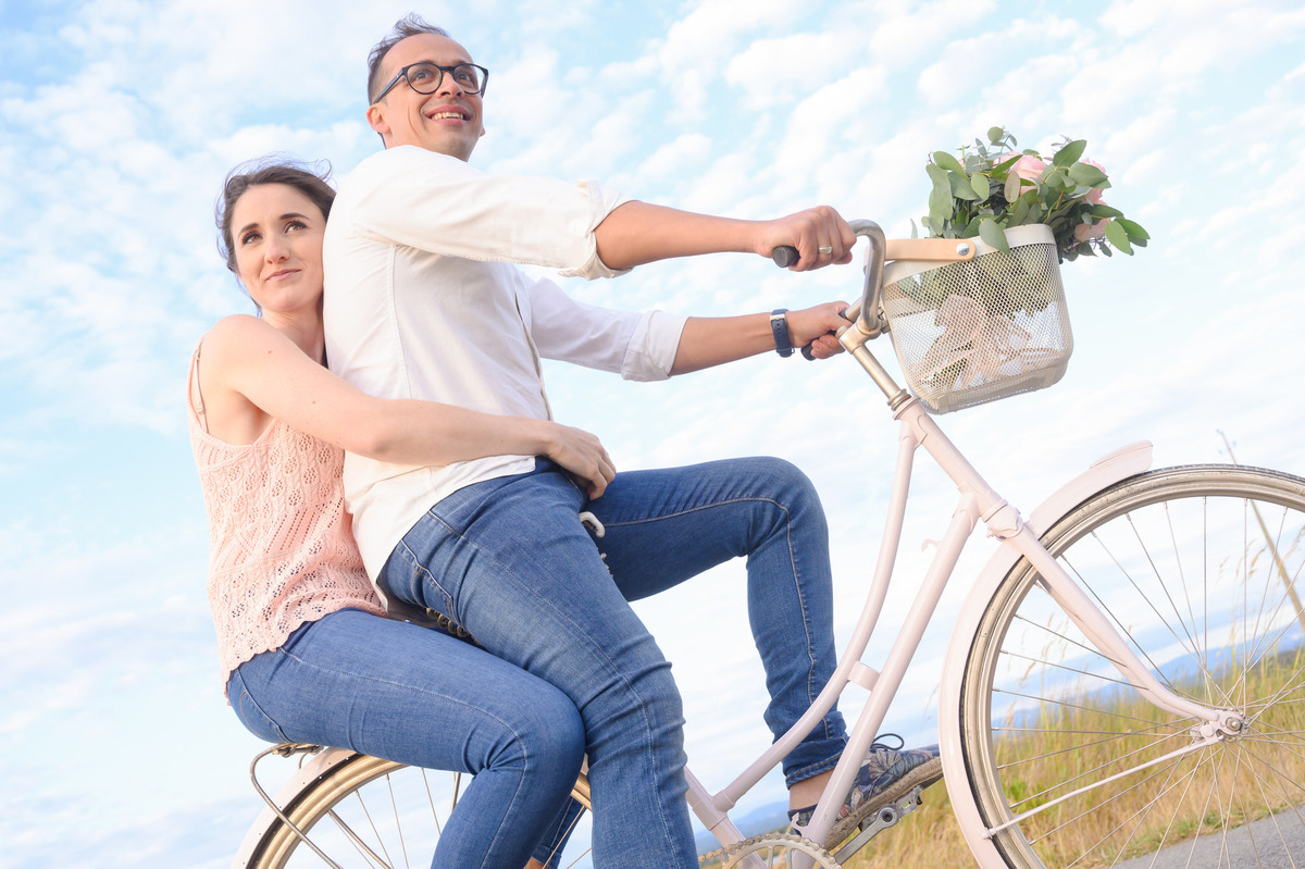 Em Ovar, casal pedala juntos sobre bicicleta branca com flores, captado por Humberto Barbosa em sessão de casamento descontraída
