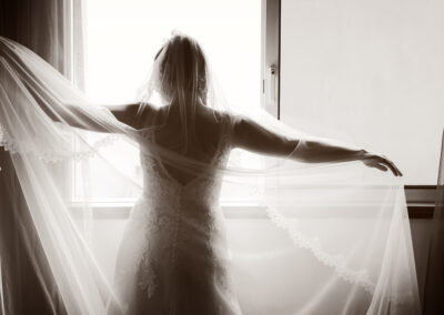 Noiva contempla a luz da janela envolvida em véu transparente — fotografia de casamento por Humberto Barbosa em Santa Maria da Feira